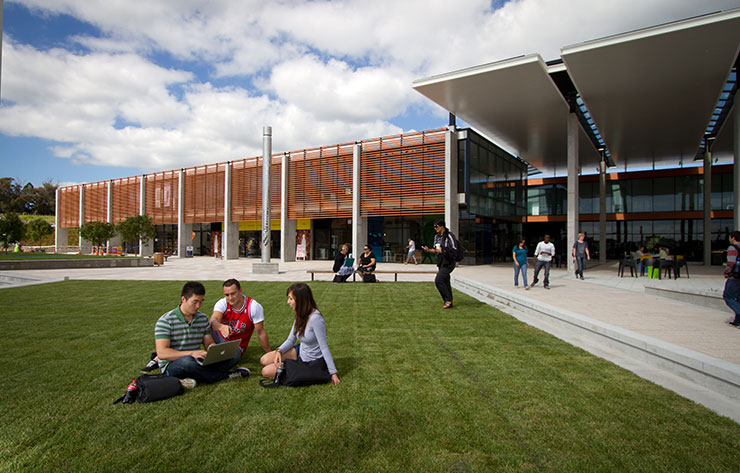 Students relaxing outside on the grass in front of large building 