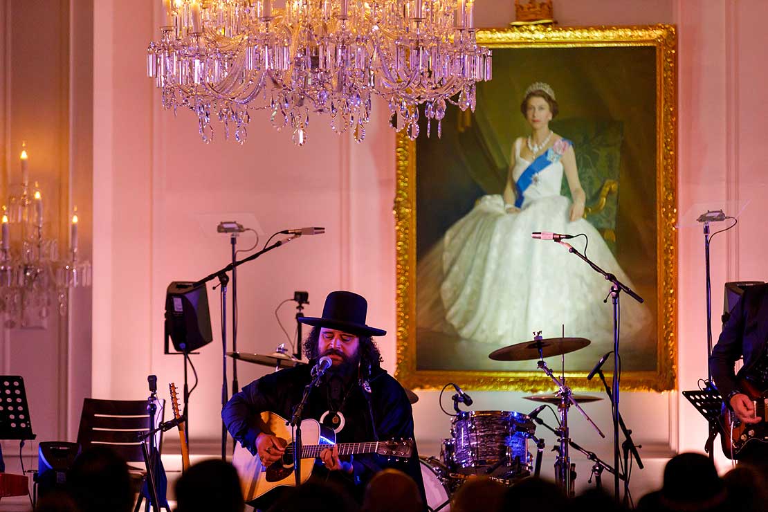 Troy Kingi performing at Government House in front of a portrait of the Queen.